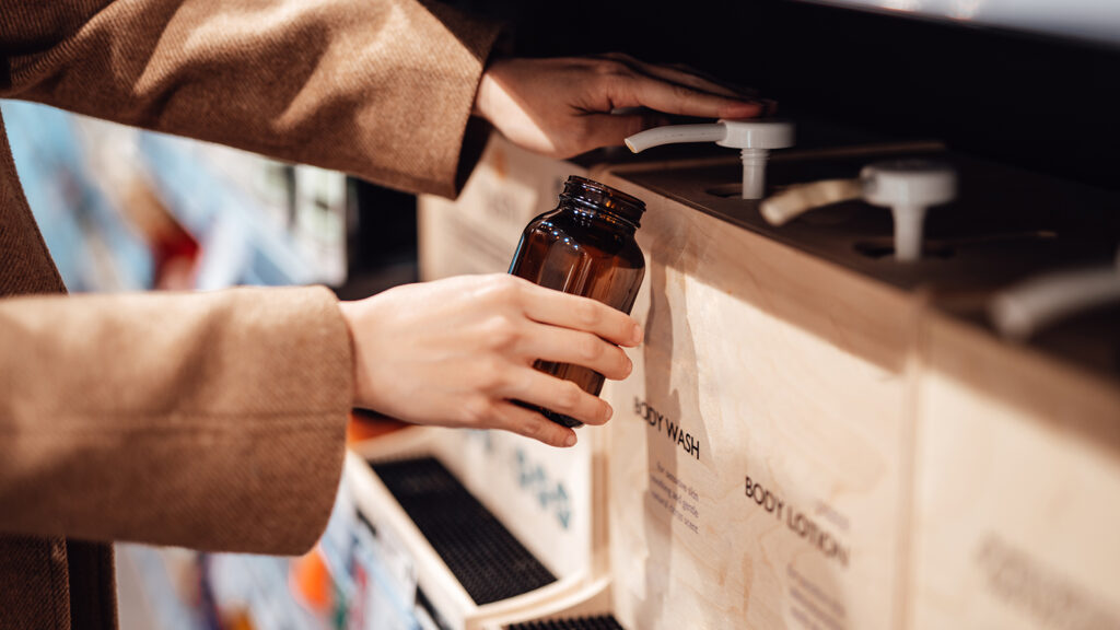 Young woman refilling shower gel / body wash into a reusable glass bottle in zero waste store