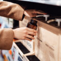 Young woman refilling shower gel / body wash into a reusable glass bottle in zero waste store