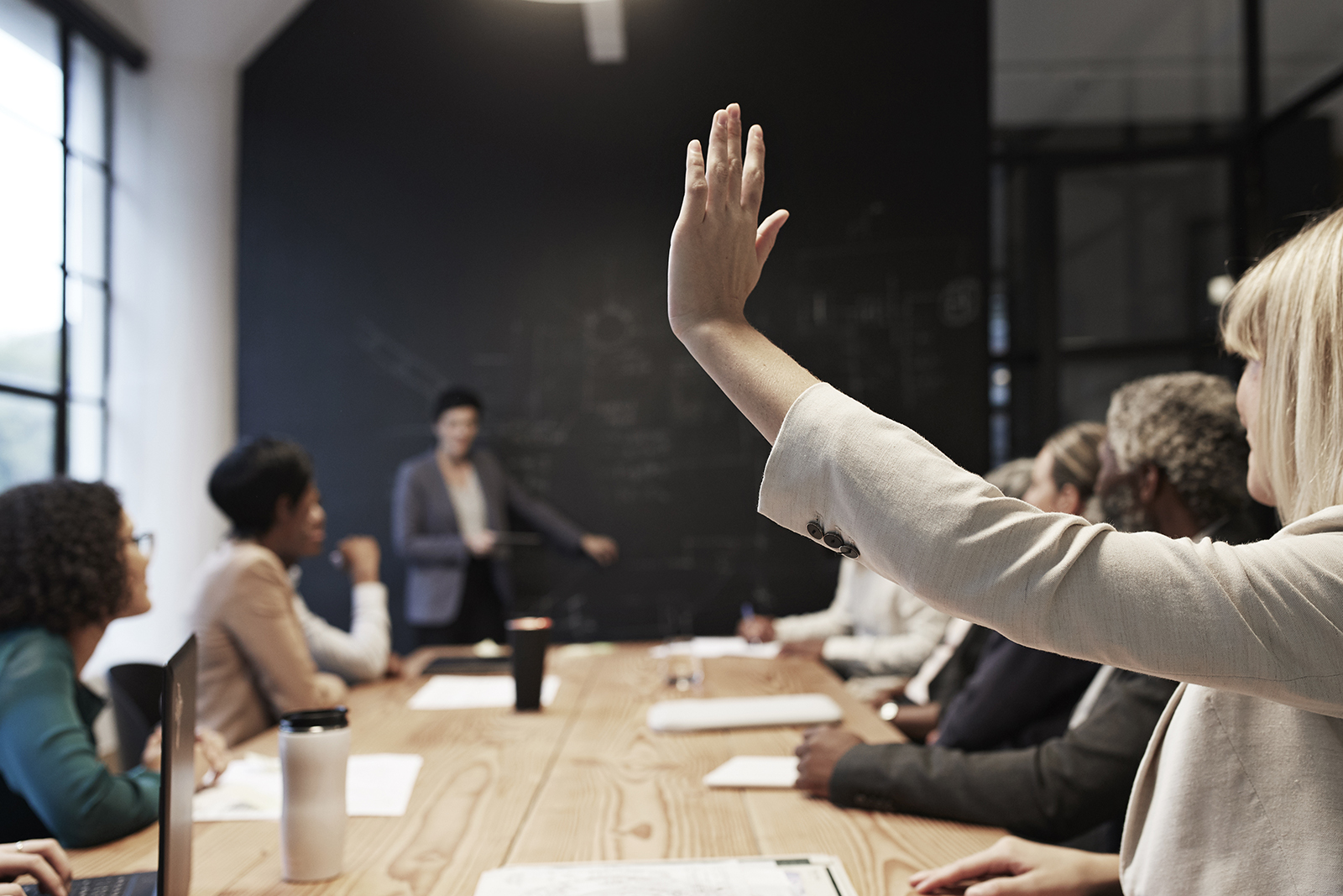 Businesswoman with hand raised sitting with male and female coworkers in conference room during office meeting