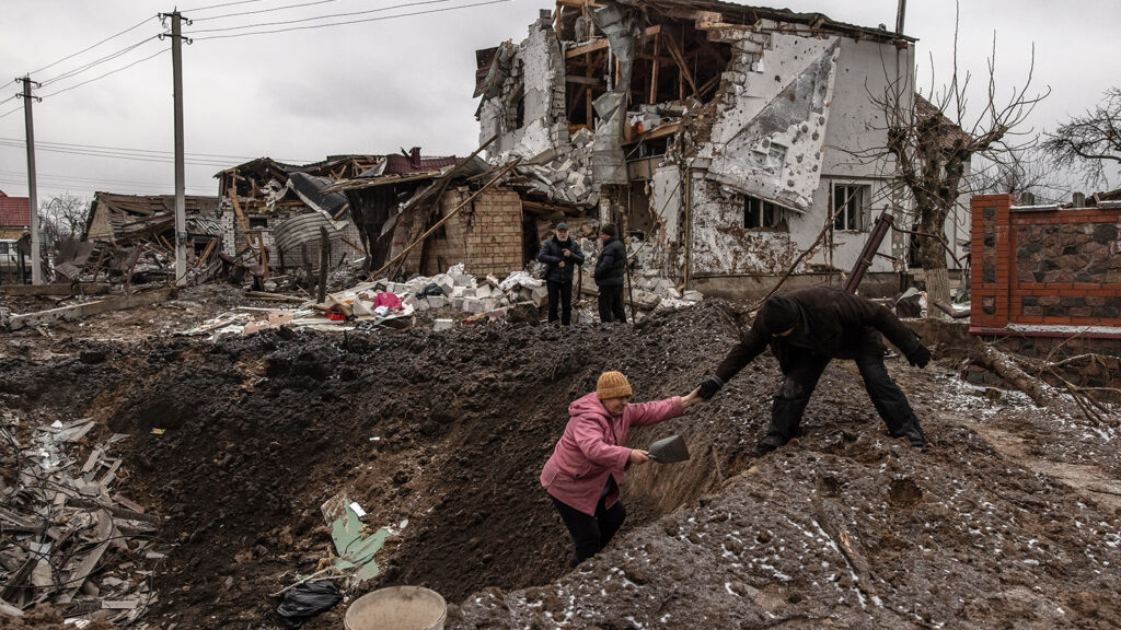 A man helps a woman to get out from a crater next to damaged residential buildings following the Russian missile attacks on January 26, 2023 in an urban-type settlement Hlevakha, outside Kyiv, Ukraine