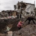 A man helps a woman to get out from a crater next to damaged residential buildings following the Russian missile attacks on January 26, 2023 in an urban-type settlement Hlevakha, outside Kyiv, Ukraine