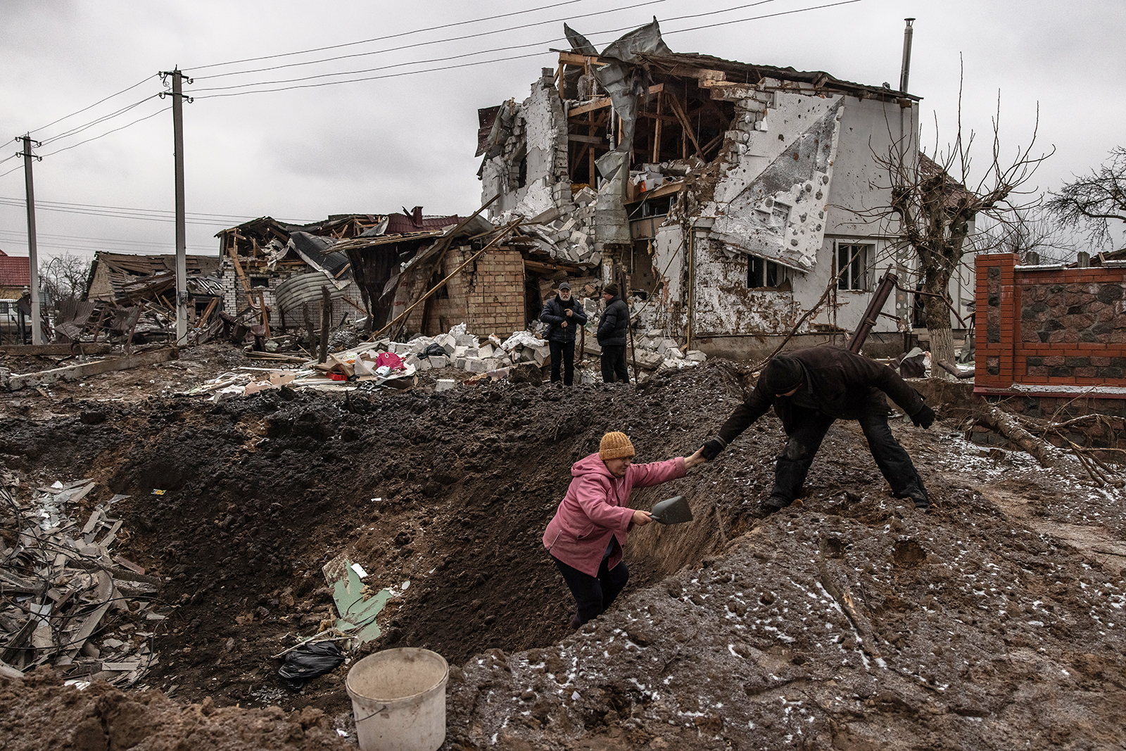 A man helps a woman to get out from a crater next to damaged residential buildings following the Russian missile attacks on January 26, 2023 in an urban-type settlement Hlevakha, outside Kyiv, Ukraine