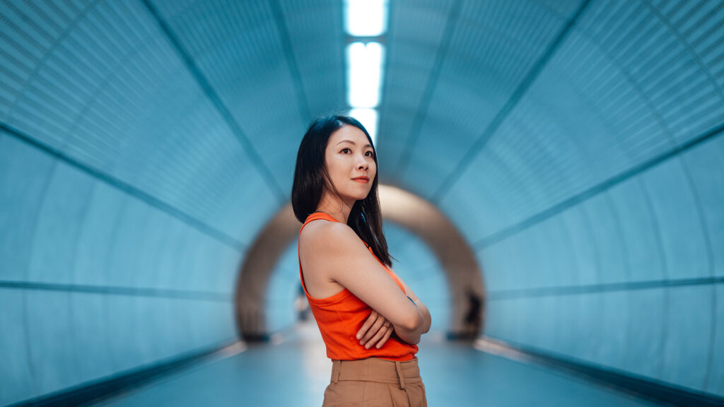 Confident young Asian woman with arms crossed, standing in modern train station