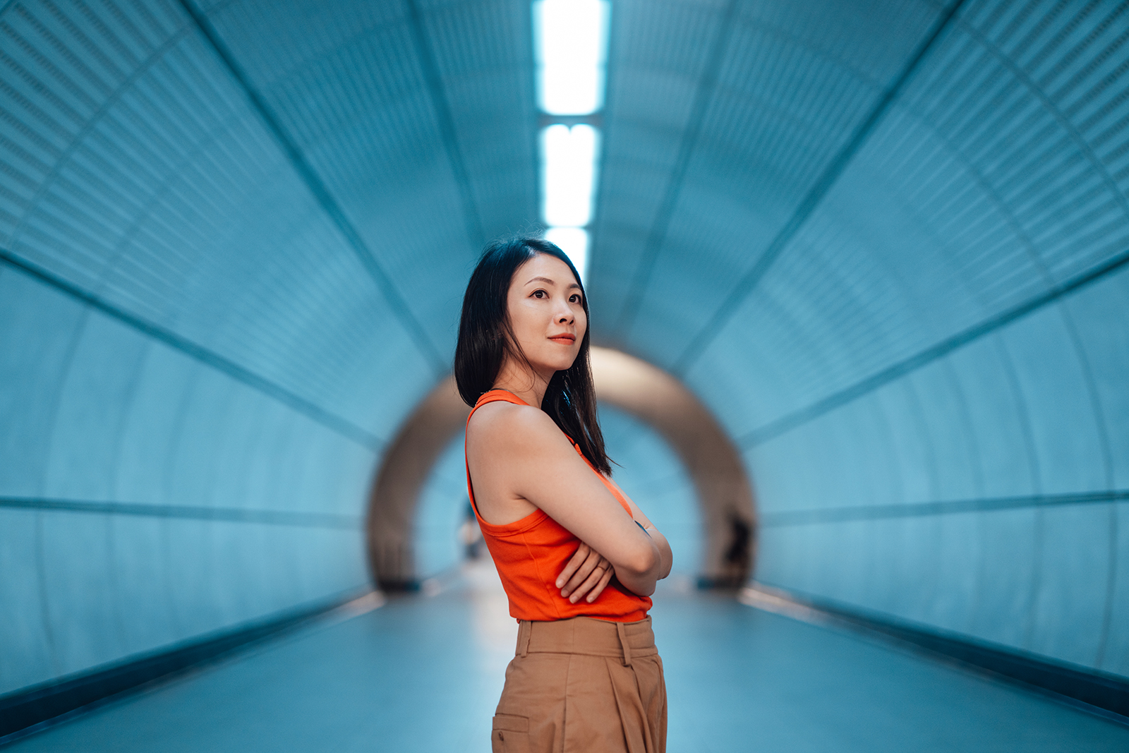 Confident young Asian woman with arms crossed, standing in modern train station